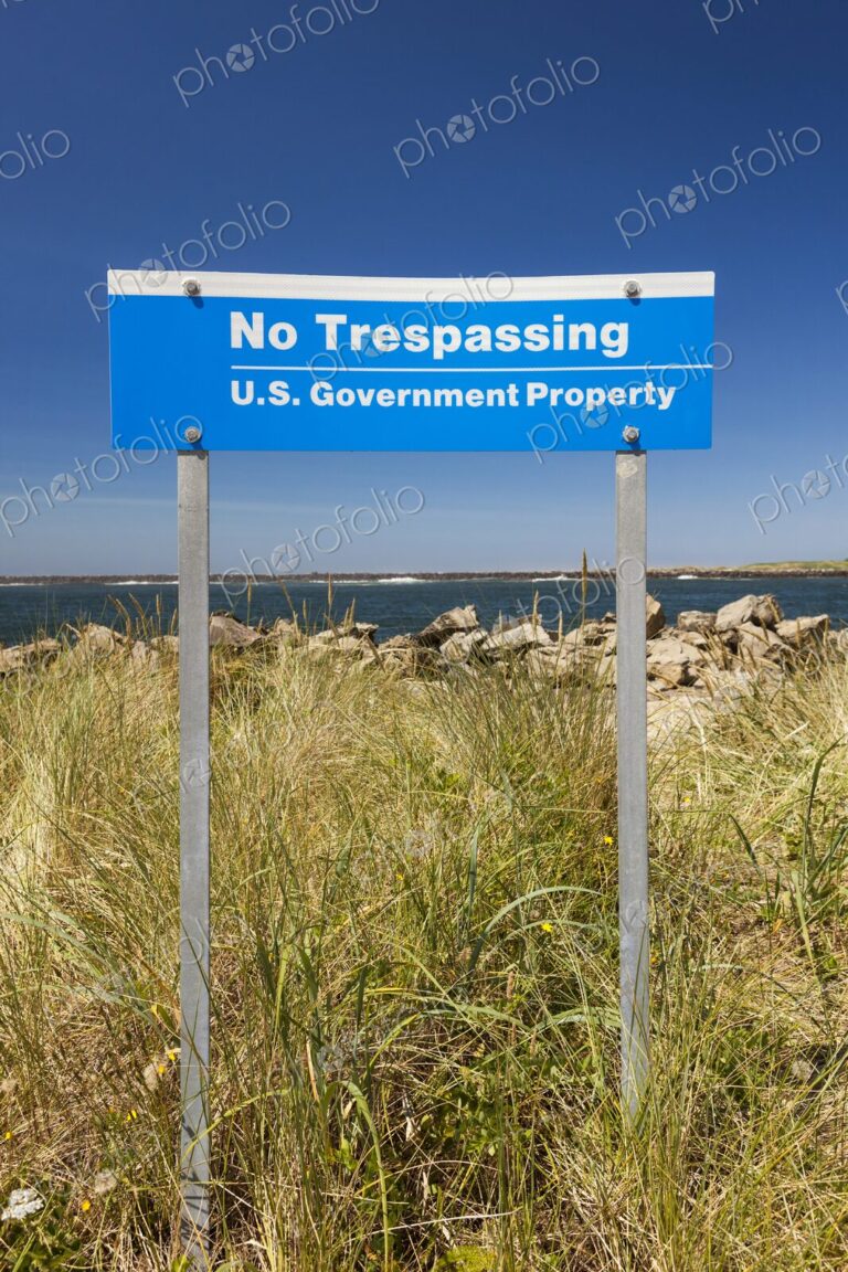 Blue "No Trespassing, U.S. Government Property" sign posted in grassy dunes near the…