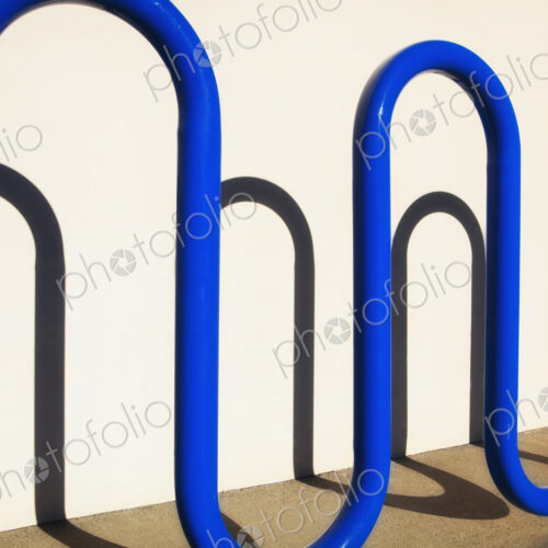 Blue curved metal bike rack throwing a shadow on the wall in Redmond, California Blue curved metal bike rack throwing a shadow on the wall in Redmond, California