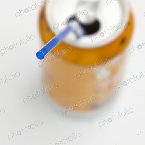 Blue straw inserted into open orange soda can with white background. Creative minimal…