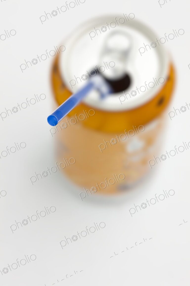Blue straw inserted into open orange soda can with white background. Creative minimal…
