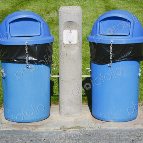 Blue trash cans on a grass sports field.