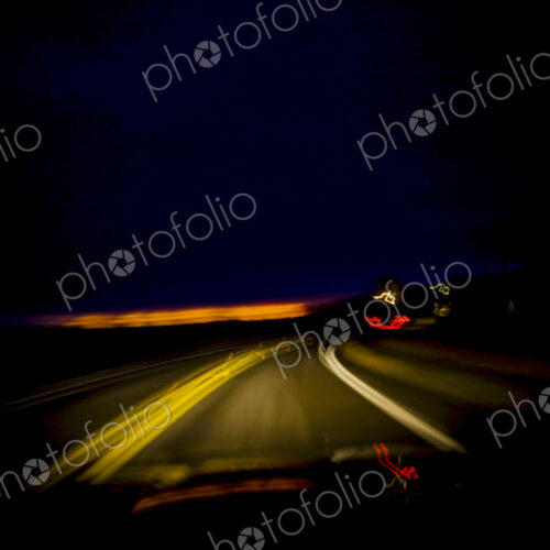 Blurred driver's view of a roadway at night through the windshield.