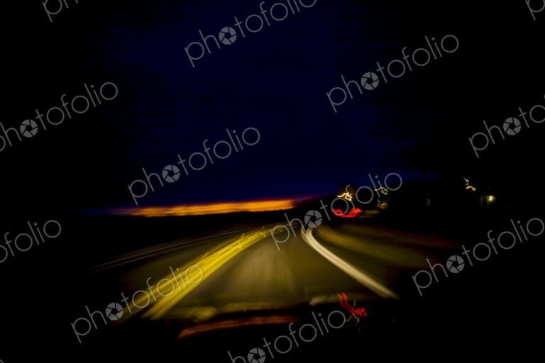 Blurred driver's view of a roadway at night through the windshield.