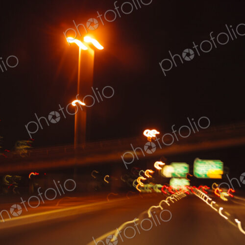 Blurred driver's view of an urban highway at night, the signs and street lights of the… Blurred driver's view of an urban highway at night, the signs and street lights of the…