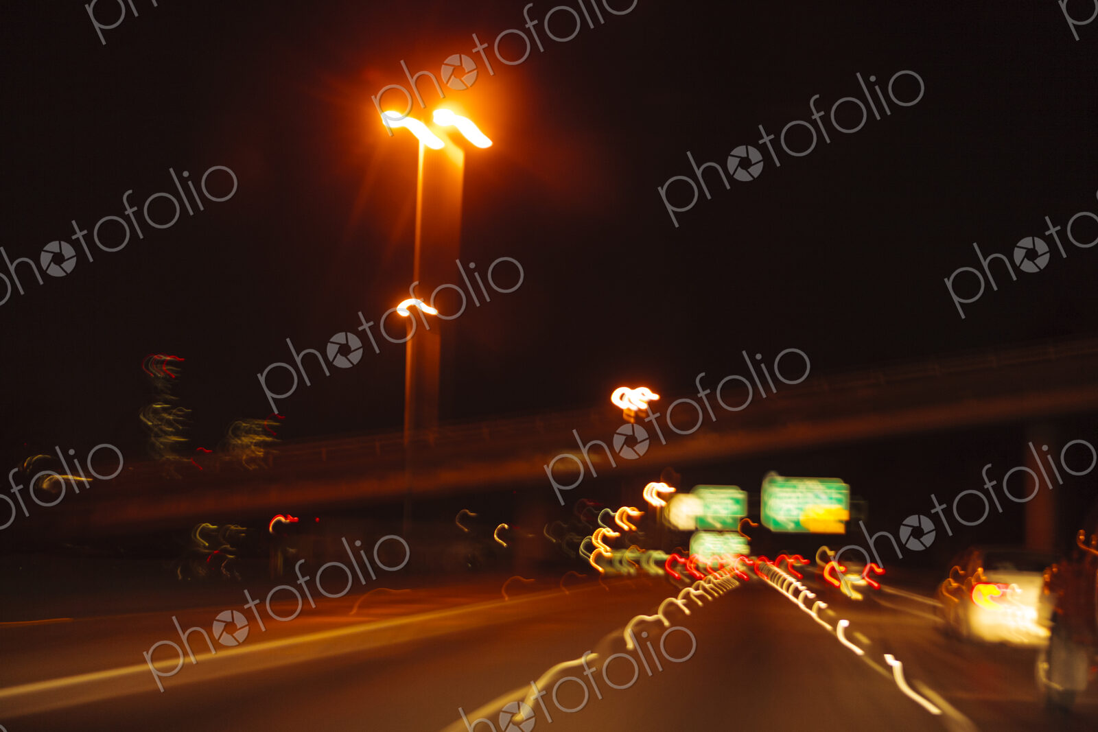 Blurred driver’s view of an urban highway at night, the signs and street lights of the…