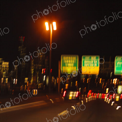 Blurred driver's view of an urban highway at night, the signs and street lights of the… Blurred driver's view of an urban highway at night, the signs and street lights of the…