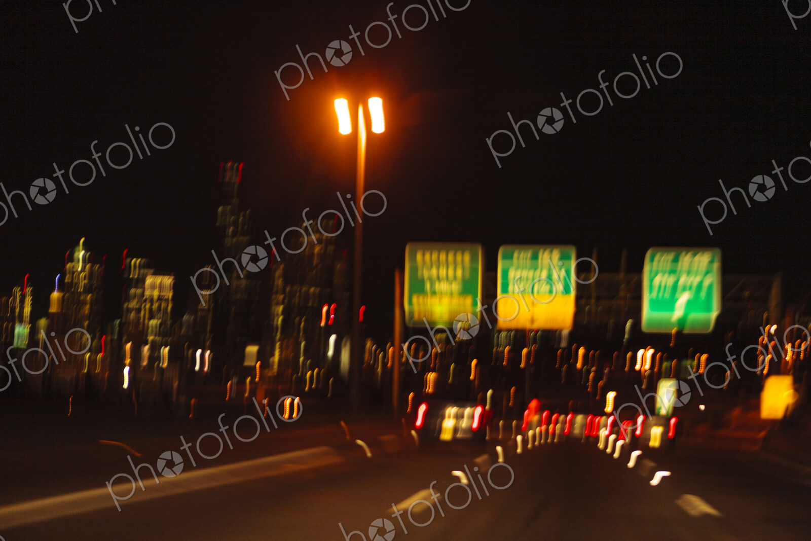 Blurred driver’s view of an urban highway at night, the signs and street lights of the…