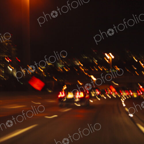 Blurred driver's view of an urban highway at night, the signs and street lights of the… Blurred driver's view of an urban highway at night, the signs and street lights of the…