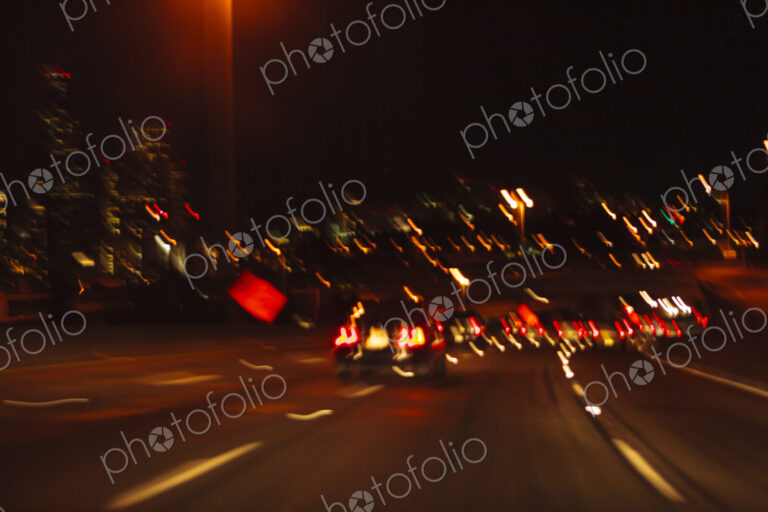 Blurred driver's view of an urban highway at night, the signs and street lights of the…