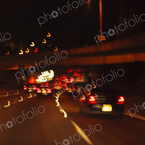 Blurred driver's view of an urban highway at night, the signs and street lights of the… Blurred driver's view of an urban highway at night, the signs and street lights of the…
