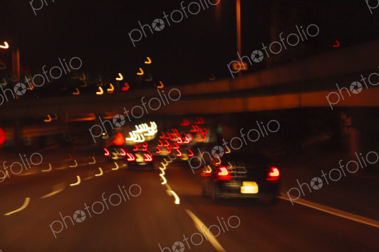 Blurred driver's view of an urban highway at night, the signs and street lights of the…