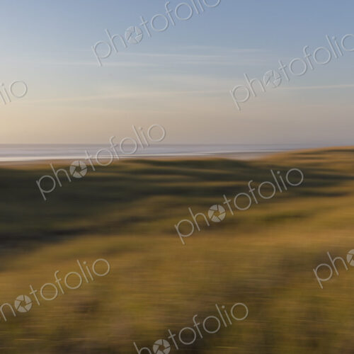 Blurred motion abstract of expansive field of beach grasses, ocean and beach in distance.