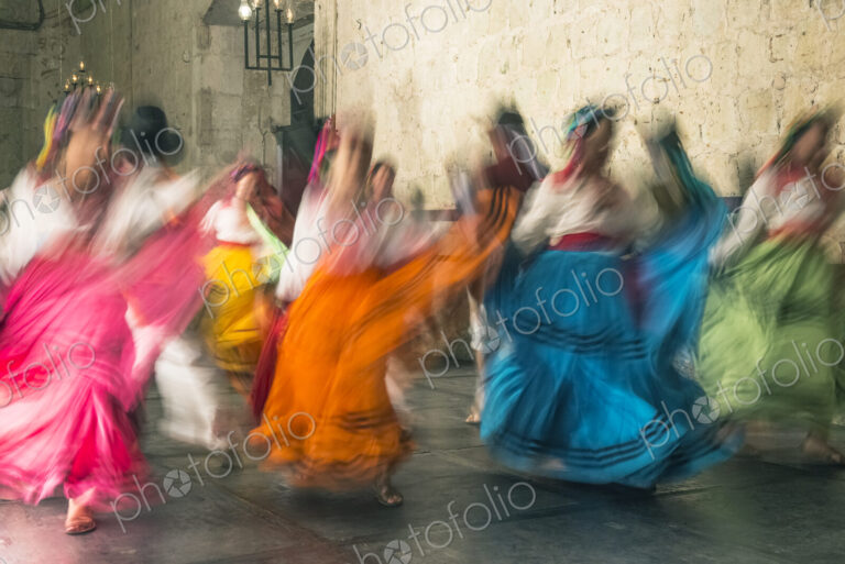 Blurred view of women dancing in traditional costumes, with bright coloured skirts
