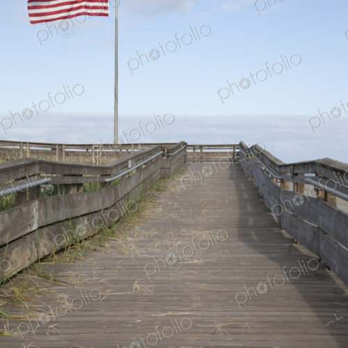 Boardwalk through grassland with mountains and American flag flying.