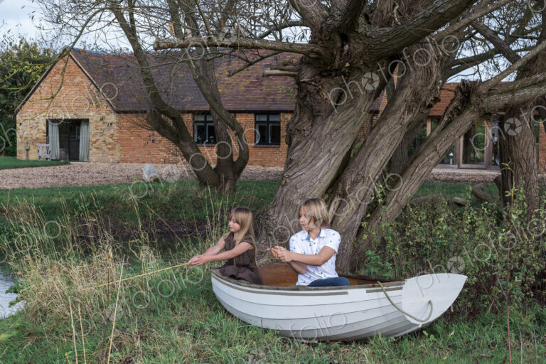 Boy and girl playing in fishing boat on land, fishing in pond by house.