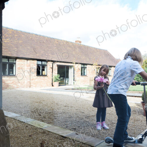 Boy and girl playing with scooter in courtyard outside house.