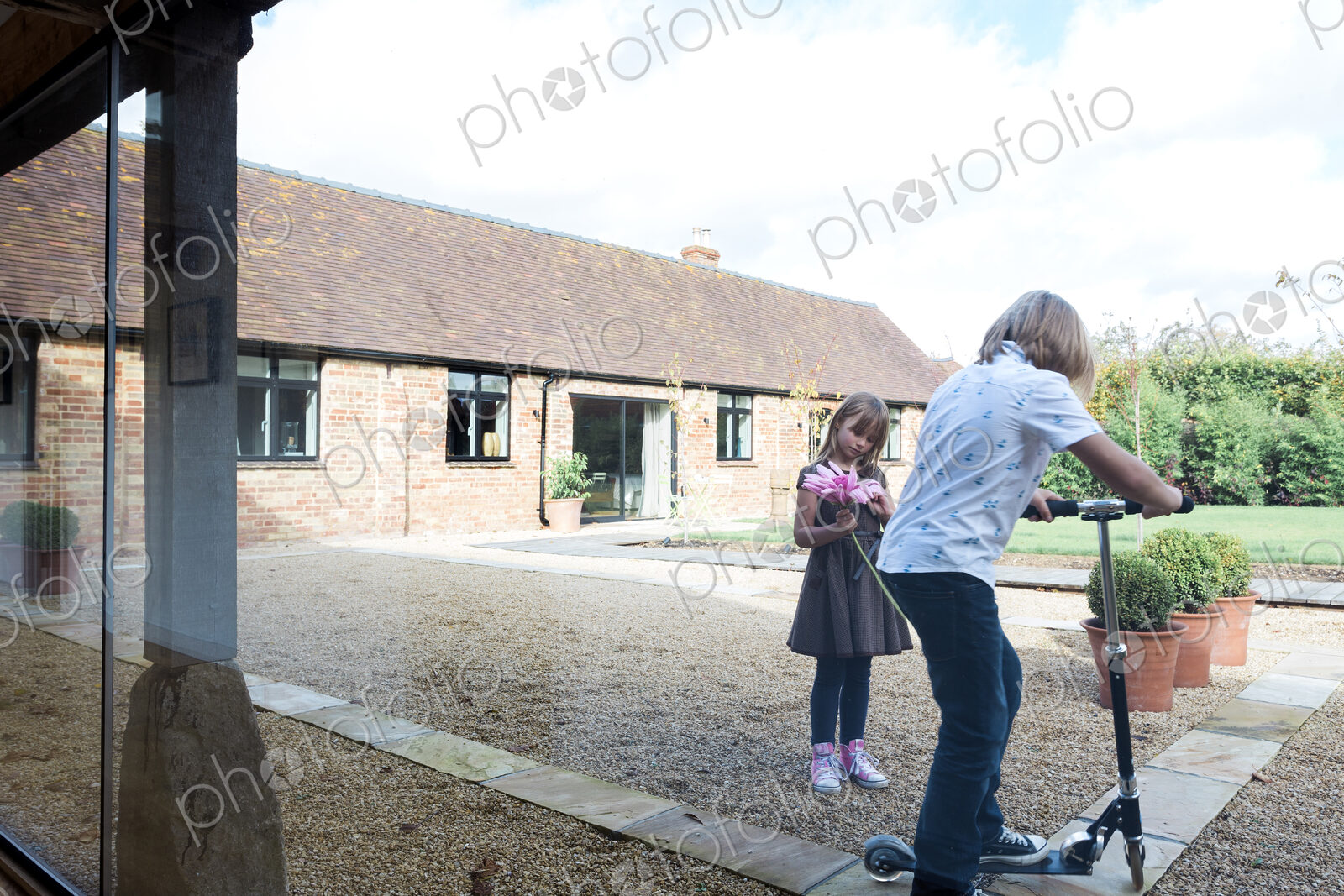 Boy and girl playing with scooter in courtyard outside house.