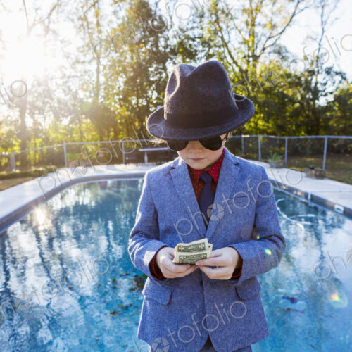 Boy in a suit and dark glasses standing on the edge of water counting dollar bills. Boy in a suit and dark glasses standing on the edge of water counting dollar bills.