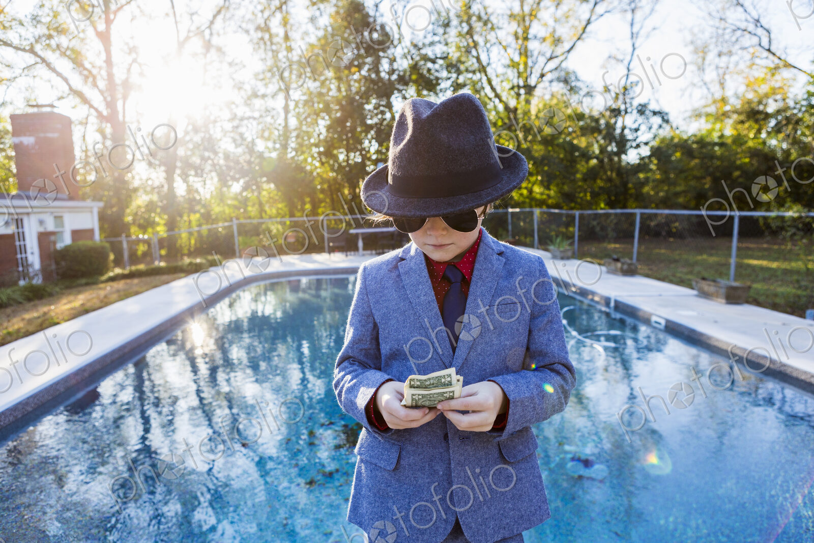 Boy in a suit and dark glasses standing on the edge of water counting dollar bills.