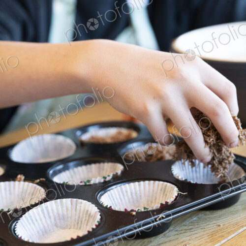 Boy's hand placing cake mix into tray in kitchen.