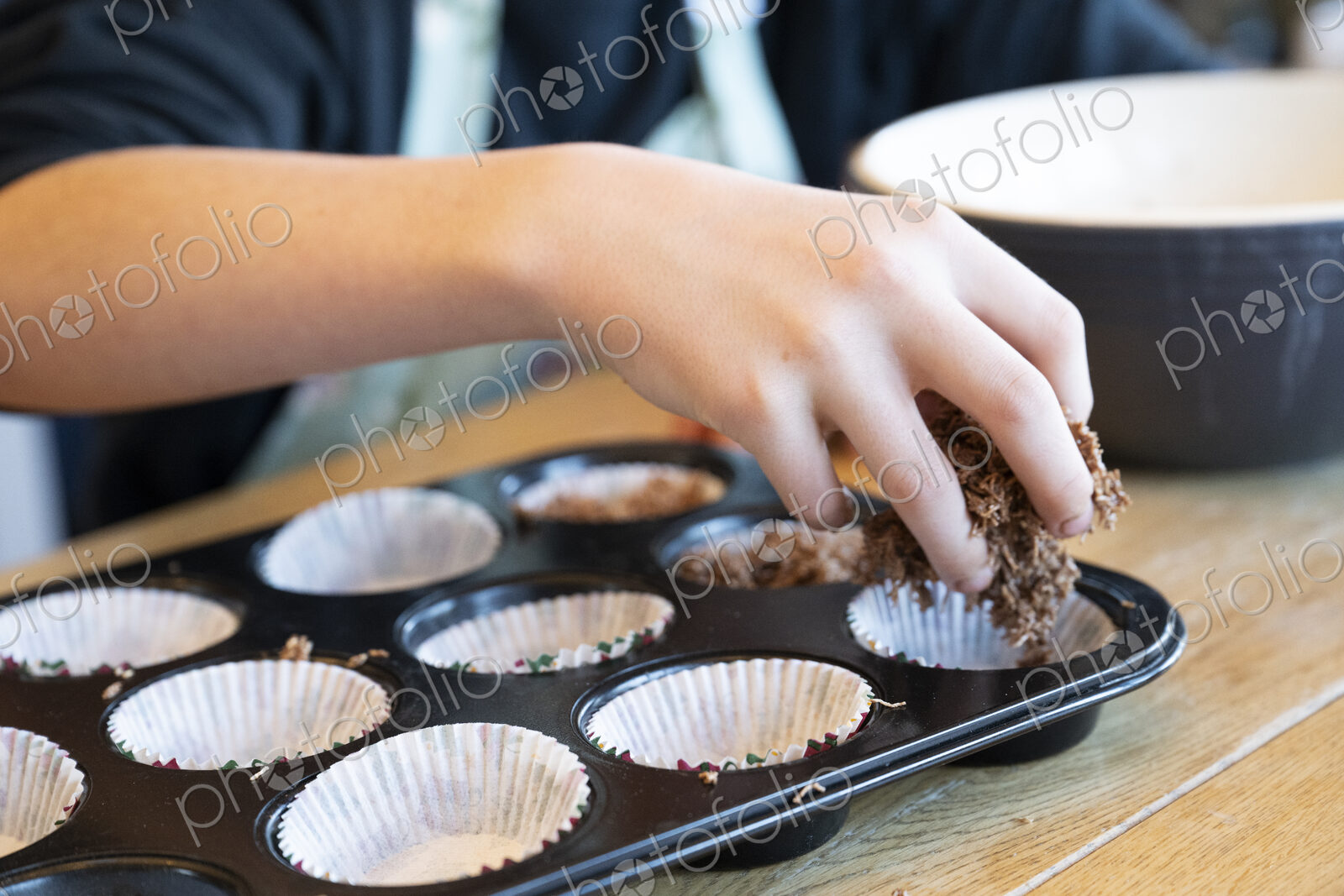 Boy’s hand placing cake mix into tray in kitchen.