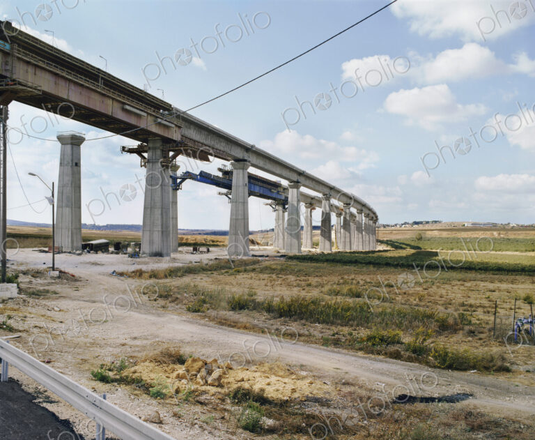 Bridge under construction, pillars and elevated road across an arid landscape.