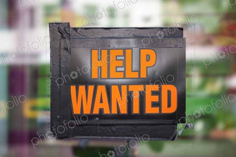 Bright orange "Help Wanted" sign taped to a window, symbolizing job opportunities,…