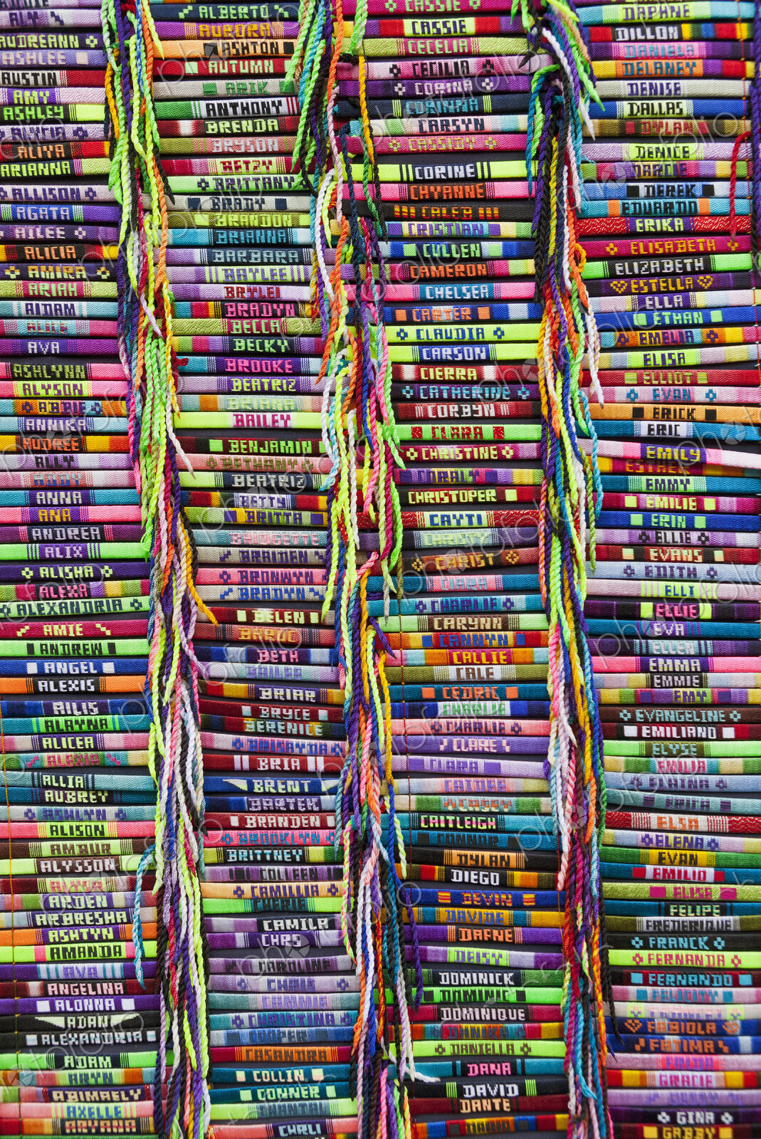 Brightly colored bracelets with embroidered names on a market stall.