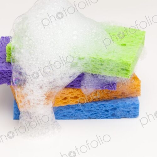 Brightly colored household sponges stacked and covered in foamy soap bubbles against a… Brightly colored household sponges stacked and covered in foamy soap bubbles against a…