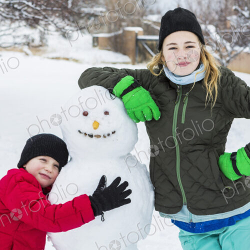 Brother and sister, a young boy and teenage girl leaning on snowman in winter Brother and sister, a young boy and teenage girl leaning on snowman in winter