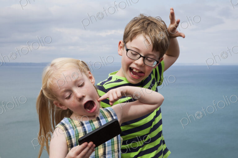 Brother and sister making faces and taking a selfie with a smart phone.