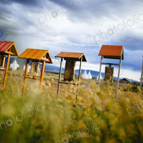 Buddhist prayer drums under small wooden roofs, monuments in the background. Buddhist prayer drums under small wooden roofs, monuments in the background.