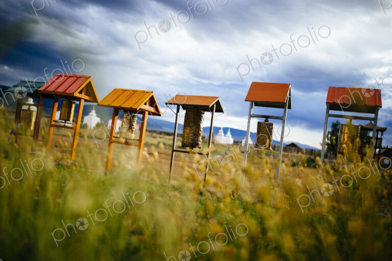 Buddhist prayer drums under small wooden roofs, monuments in the background.
