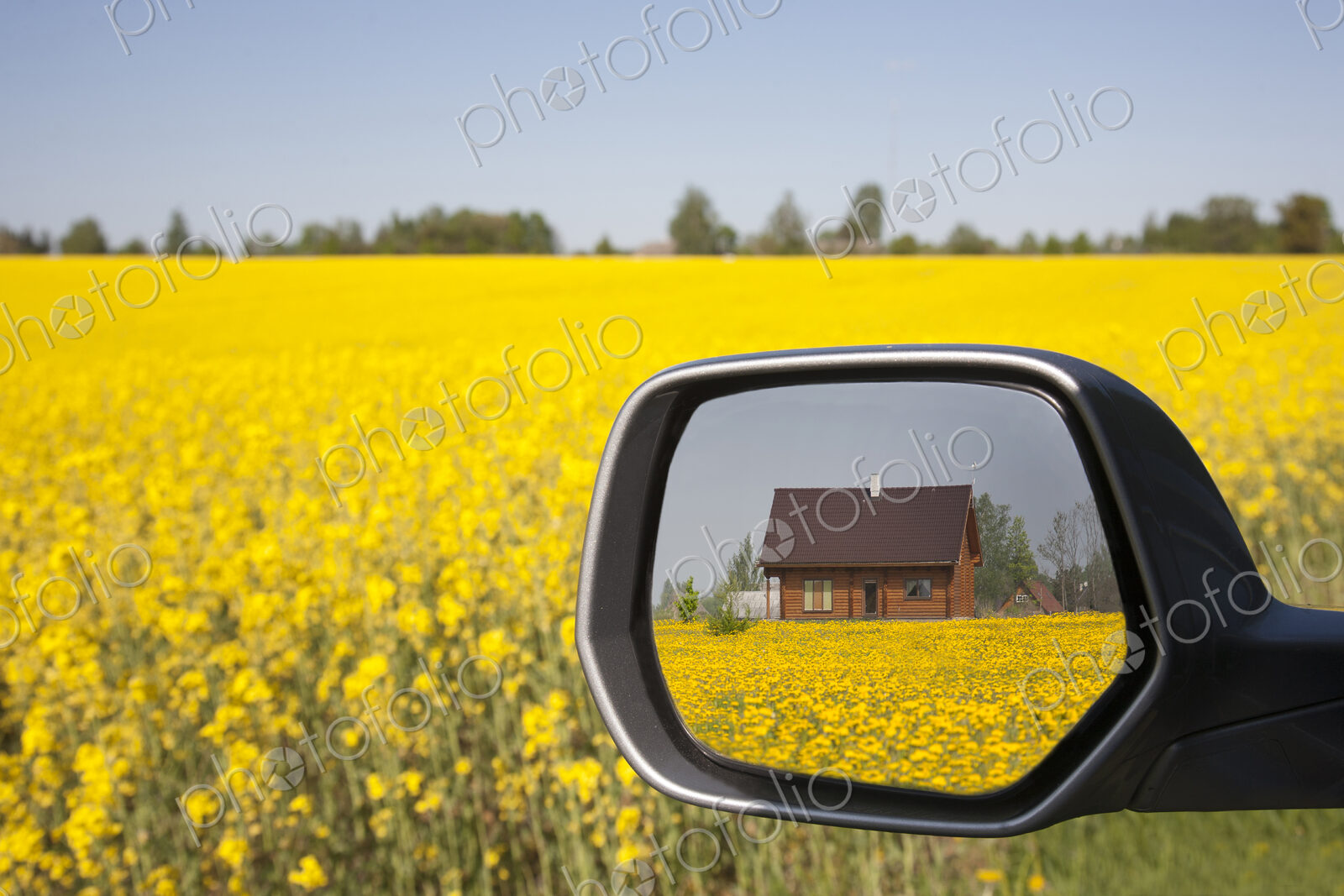 Building viewed in car side wing mirror, yellow flowering oil seed rape field and…