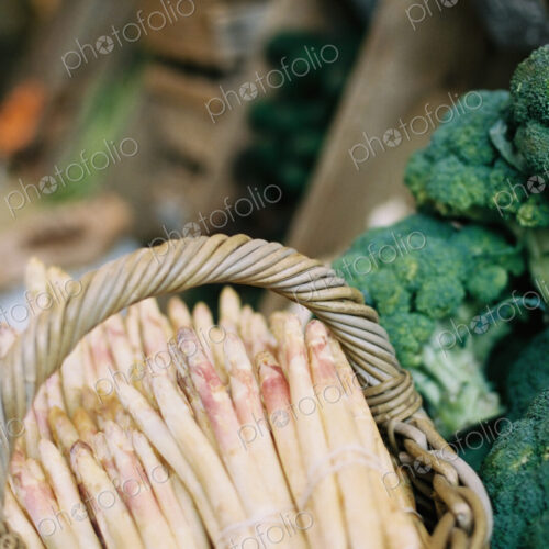 Bundles of white asparagus and broccoli florets on a vegetable stall.