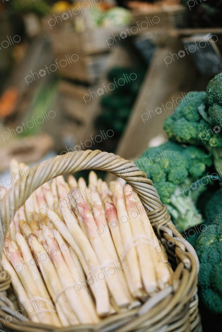 Bundles of white asparagus and broccoli florets on a vegetable stall.