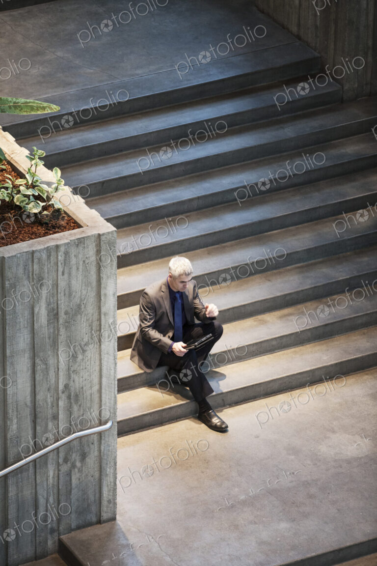 Busienssman working on a notebook computer while sitting on the steps of a convention…