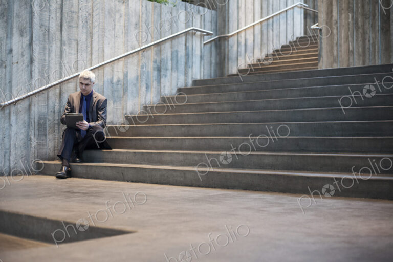 Busienssman working on a notebook computer while sitting on the steps of a convention…