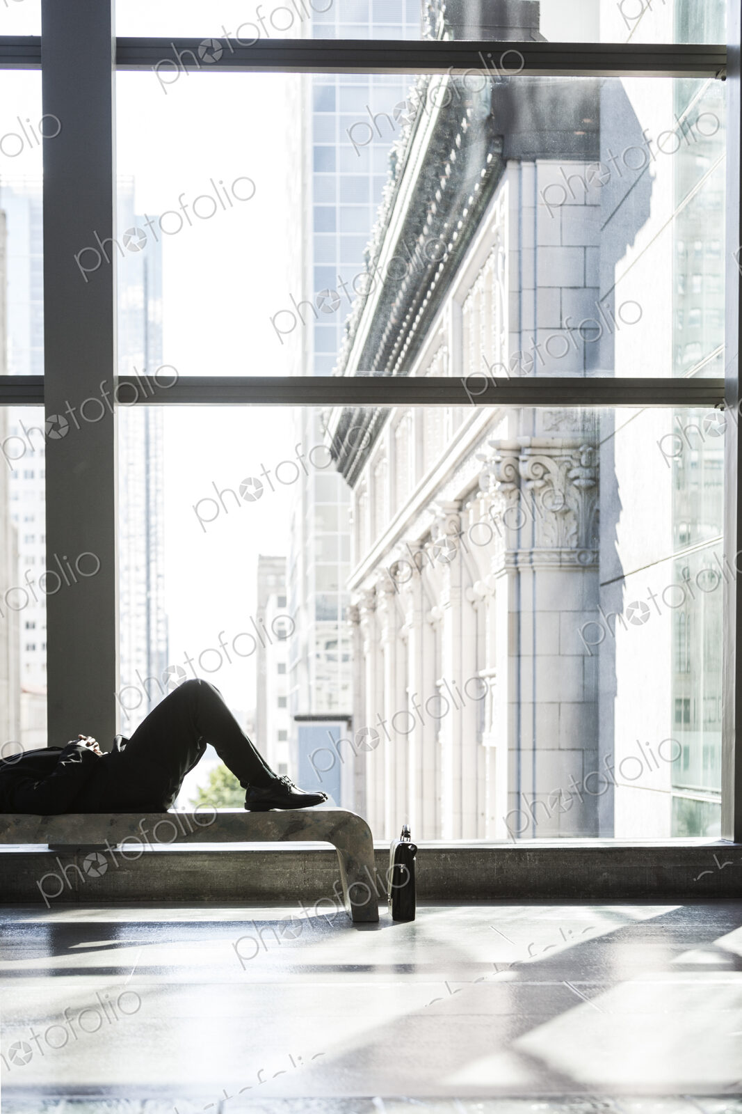 Business man taking a break laying on a bench in a large open lobby area.