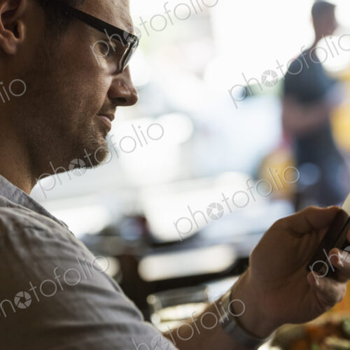 Business on the go. A man sitting at a cafe table, using his mobile phone. Looking… Business on the go. A man sitting at a cafe table, using his mobile phone. Looking…