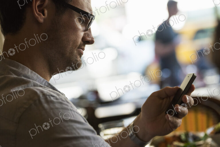 Business on the go. A man sitting at a cafe table, using his mobile phone. Looking…