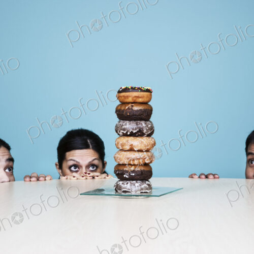 Business people hiding behind a table with a stack of doughnuts on it. Business people hiding behind a table with a stack of doughnuts on it.