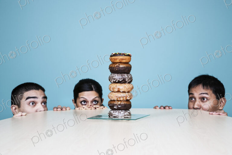 Business people hiding behind a table with a stack of doughnuts on it.