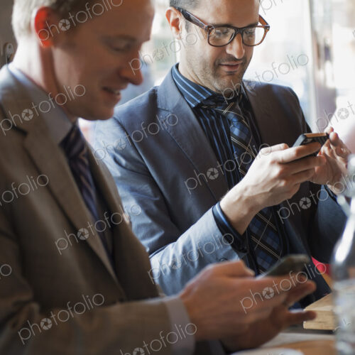 Business people in the city. Two men sitting at a cafe table checking their mobile… Business people in the city. Two men sitting at a cafe table checking their mobile…