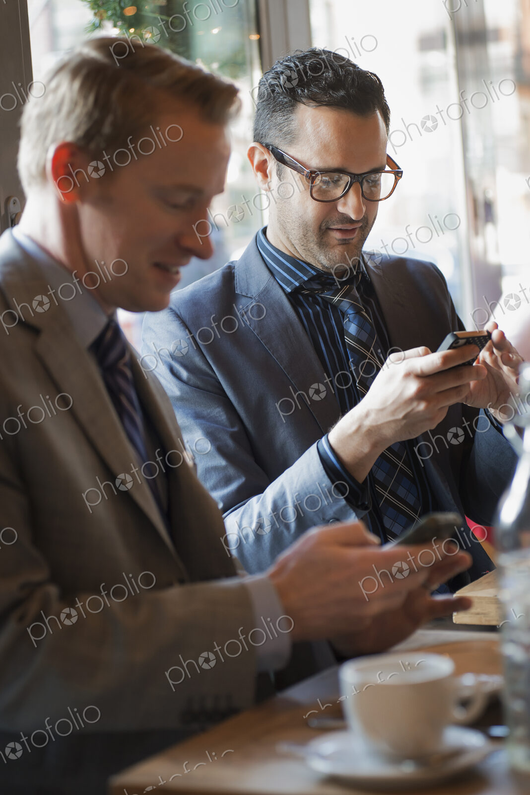 Business people in the city. Two men sitting at a cafe table checking their mobile…