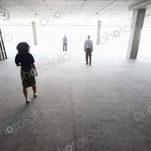 Business people walking toward windows in a large empty office raw space.