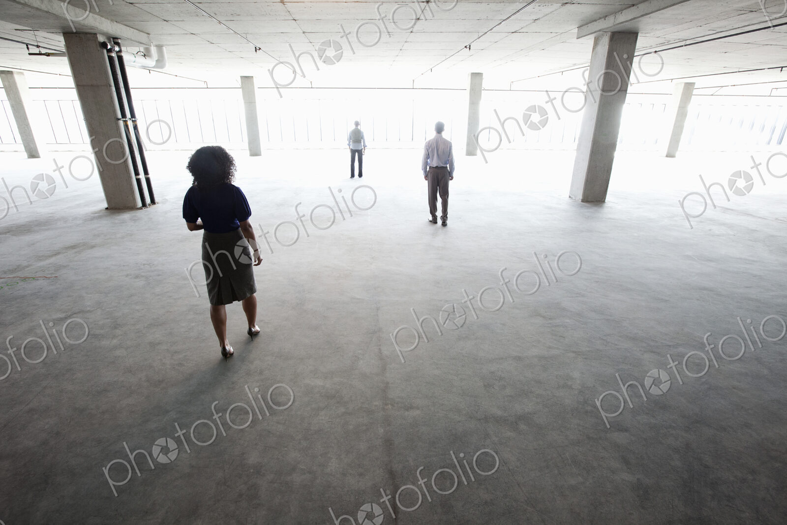 Business people walking toward windows in a large empty office raw space.