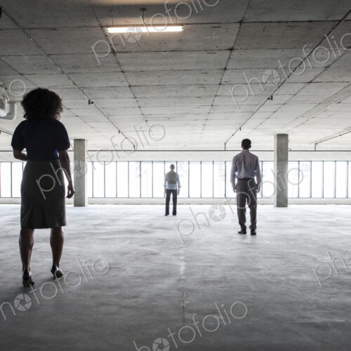 Business people walking toward windows in a large empty office raw space.