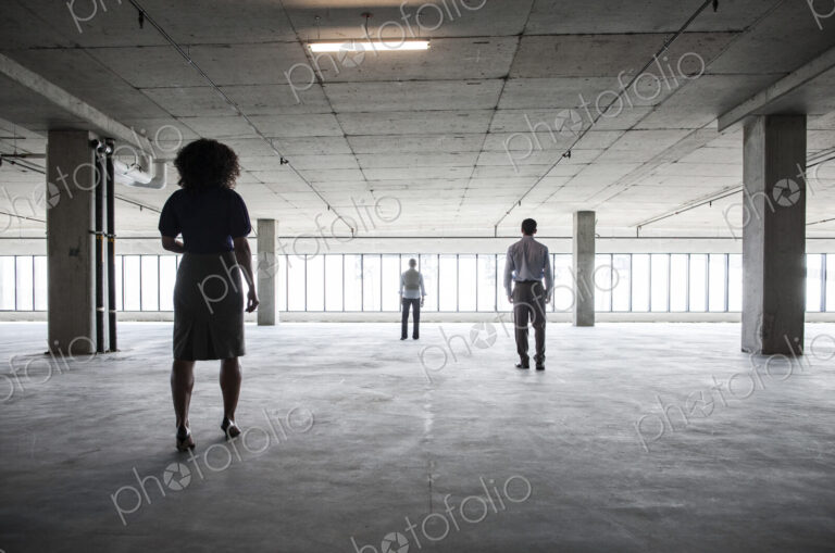 Business people walking toward windows in a large empty office raw space.