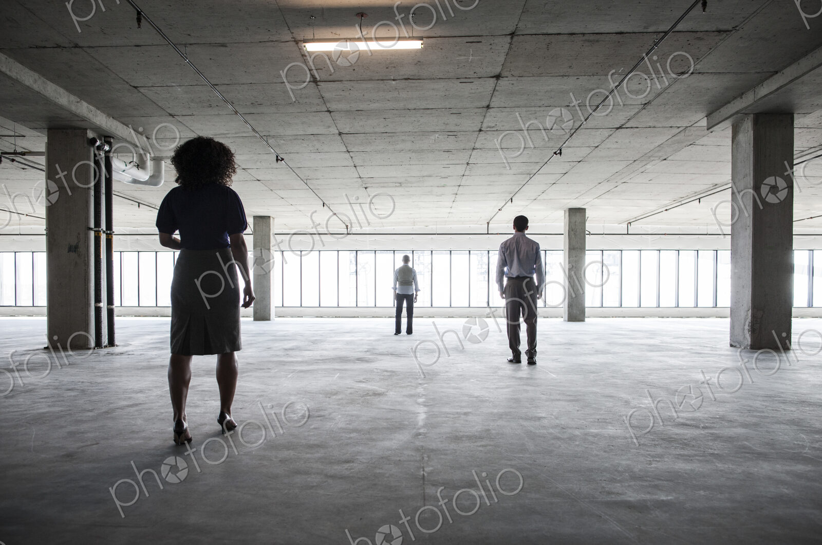 Business people walking toward windows in a large empty office raw space.